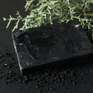 Charcoal soap and thuja branches on black background